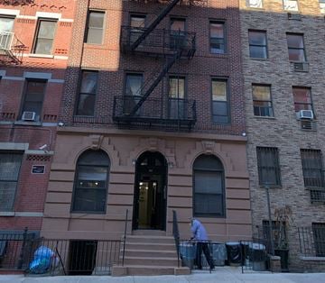 New York apartment for rent - A man is sweeping the sidewalk in front of a brown building with a black fire escape.