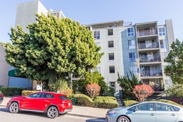 Oakland apartment for rent - A red car is parked in front of a silver car and a building.