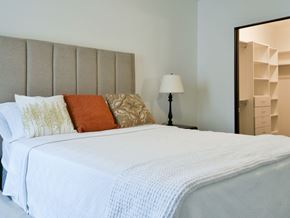 Minneapolis apartment for rent - A bed with a white comforter and pillows with a lamp and a mirror in the background.