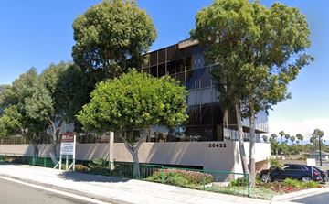 Huntington Beach apartment for rent - A modern building with a glass facade and a sign that reads "20422" is surrounded by trees and a green fence.