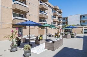Oakland apartment for rent - A patio area with a white couch, green umbrella, and potted plants.