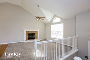 Raymore house for rent - a landing with a white railing and a ceiling fan and a fireplace