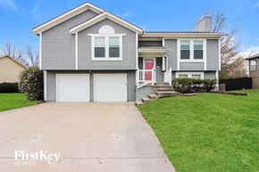 Raymore house for rent - a blue house with a white garage door and a green lawn