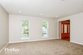 Wildwood house for rent - A room with a carpet floor, two windows, and a wooden door.