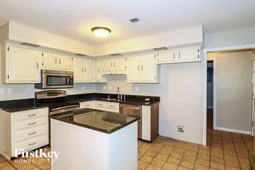 Collierville house for rent - a kitchen with white cabinets and black counter tops