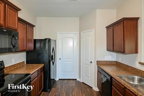 Dallas house for rent - a kitchen with brown cabinets and black appliances and a white door