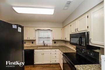 Greensboro house for rent - a kitchen with white cabinets and granite counter tops and black appliances