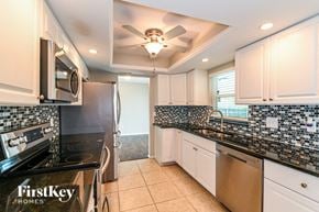 Cape Coral house for rent - a kitchen with black counters and white cabinets and a ceiling fan