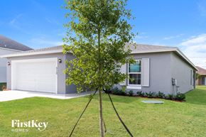 Port St. Lucie house for rent - A tree stands in the front yard of a grey house with a white garage door.