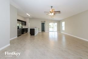 Port St. Lucie house for rent - A spacious empty room with a ceiling fan and a kitchen area in the background.