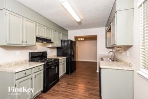 Acworth house for rent - a kitchen with white cabinets and black appliances and a wood floor