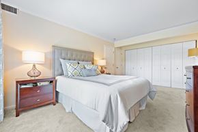 Lisle apartment for rent - A bedroom with a large bed, a nightstand with a lamp, and a dresser with a mirror.