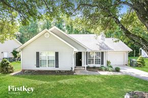 Greensboro house for rent - A house with a white siding and a black door is surrounded by greenery.
