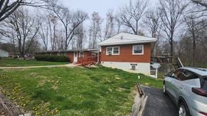 Goshen apartment for rent - A house with a red brick exterior and a white roof is surrounded by a grassy area and trees.