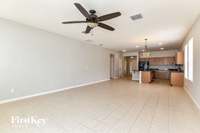 Kissimmee house for rent - A spacious empty room with a ceiling fan and a kitchen area in the background.