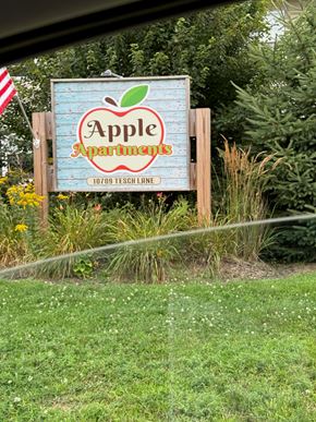 Rothschild apartment for rent - A sign for Apple Apartments is displayed in front of a grassy area.