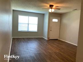 Mckinney house for rent - an empty living room with a white door and a ceiling fan