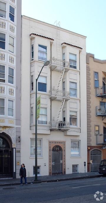 San Francisco apartment for rent - A person stands on a street in front of a white building with a fire escape.