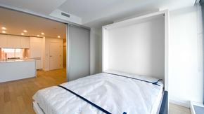 Vancouver apartment for rent - A bedroom with a bed, a window, and a kitchen area in the background.
