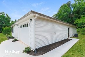Dacula house for rent - A white house with a brown roof and a garage door is surrounded by greenery.