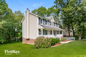 Alabaster house for rent - A house with a white porch and a brick chimney is surrounded by greenery.