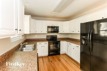 Kannapolis house for rent - a kitchen with white cabinets and black appliances