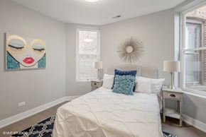 Chicago apartment for rent - A bedroom with a white bed and a painting of a woman's face on the wall.