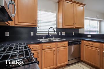 Houston house for rent - a kitchen with wooden cabinets and black countertops and a stove and sink