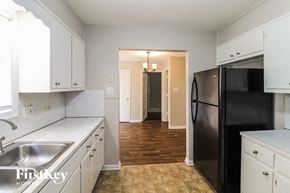 Conyers house for rent - a kitchen with white cabinets and stainless steel appliances and a hallway with a black refrigerator