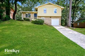 Ellenwood house for rent - A yellow house with a white garage door is surrounded by green grass and trees.