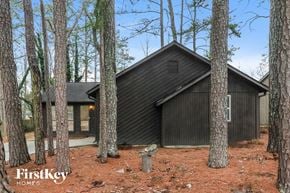 Austell house for rent - A black house with a triangular roof is nestled among tall trees.