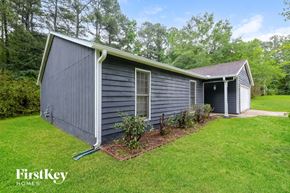 Riverdale house for rent - A small house with a grey roof and a white door is surrounded by greenery.