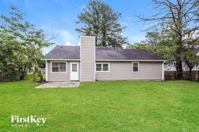 Jonesboro house for rent - A house with a grey siding and a white door is surrounded by a grassy lawn and trees.