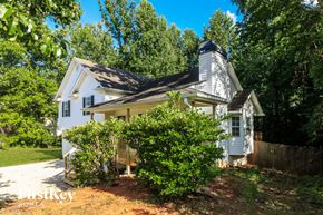 Dallas house for rent - A white house with a black roof and a chimney is surrounded by greenery.