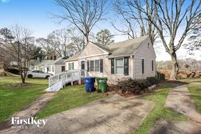 Atlanta house for rent - a small house with a white porch and a driveway with trash cans