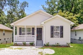 Greensboro house for rent - A white house with a black door and windows surrounded by greenery.