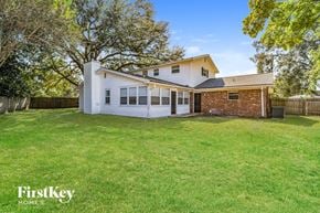 Jacksonville house for rent - A house with a white exterior and a brick chimney is surrounded by a grassy yard and trees.