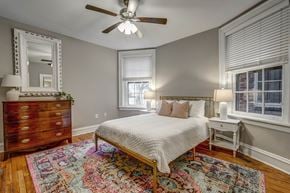 Richmond apartment for rent - A bedroom with a white bed, a wooden dresser, and a ceiling fan.