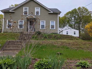 West Warwick apartment for rent - A house with a grey roof and white windows is surrounded by greenery.