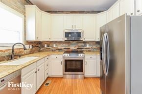 Greensboro house for rent - a kitchen with white cabinets and stainless steel appliances and a wooden floor
