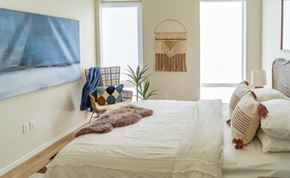 Denver apartment for rent - A bedroom with a bed, a chair, a plant, and a wall hanging.