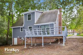 Trinity house for rent - A house with a grey exterior and a balcony is surrounded by trees.
