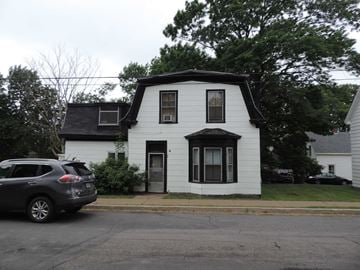 New Glasgow apartment for rent - A white house with a black door and windows is surrounded by trees.