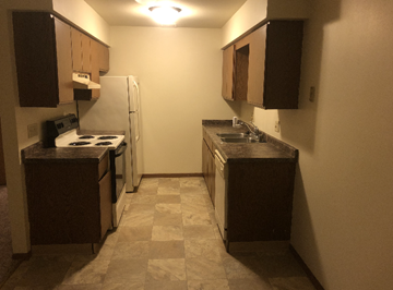 West Bend apartment for rent - A kitchen with a white refrigerator, black countertops, and brown cabinets.