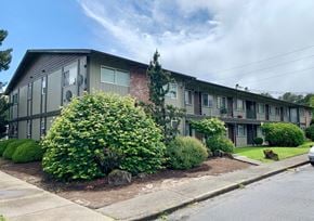 Kelso apartment for rent - A building with grey siding and a red brick chimney is surrounded by green bushes.