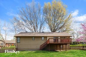 Kansas City house for rent - A house with a brown roof and a balcony is surrounded by a green lawn and trees.