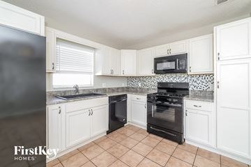 Haines City house for rent - a kitchen with white cabinets and black appliances