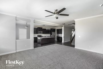 Statesville house for rent - A spacious living room with a grey carpet and a ceiling fan.