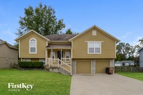 Raymore house for rent - a yellow house with a driveway and a lawn