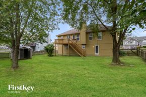 Raymore house for rent - the backyard of a yellow house with a yard and trees